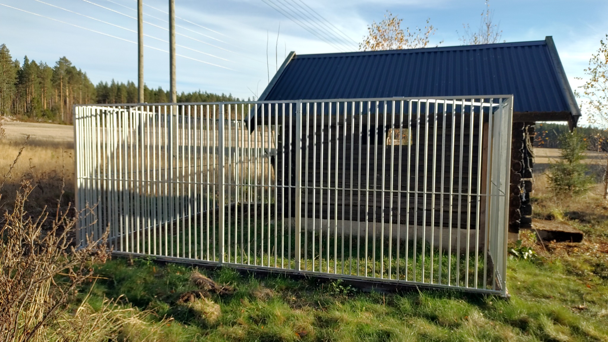 Stor Femunden Spil hundegård med loddrette spiler ved en mørk tømmerhytte